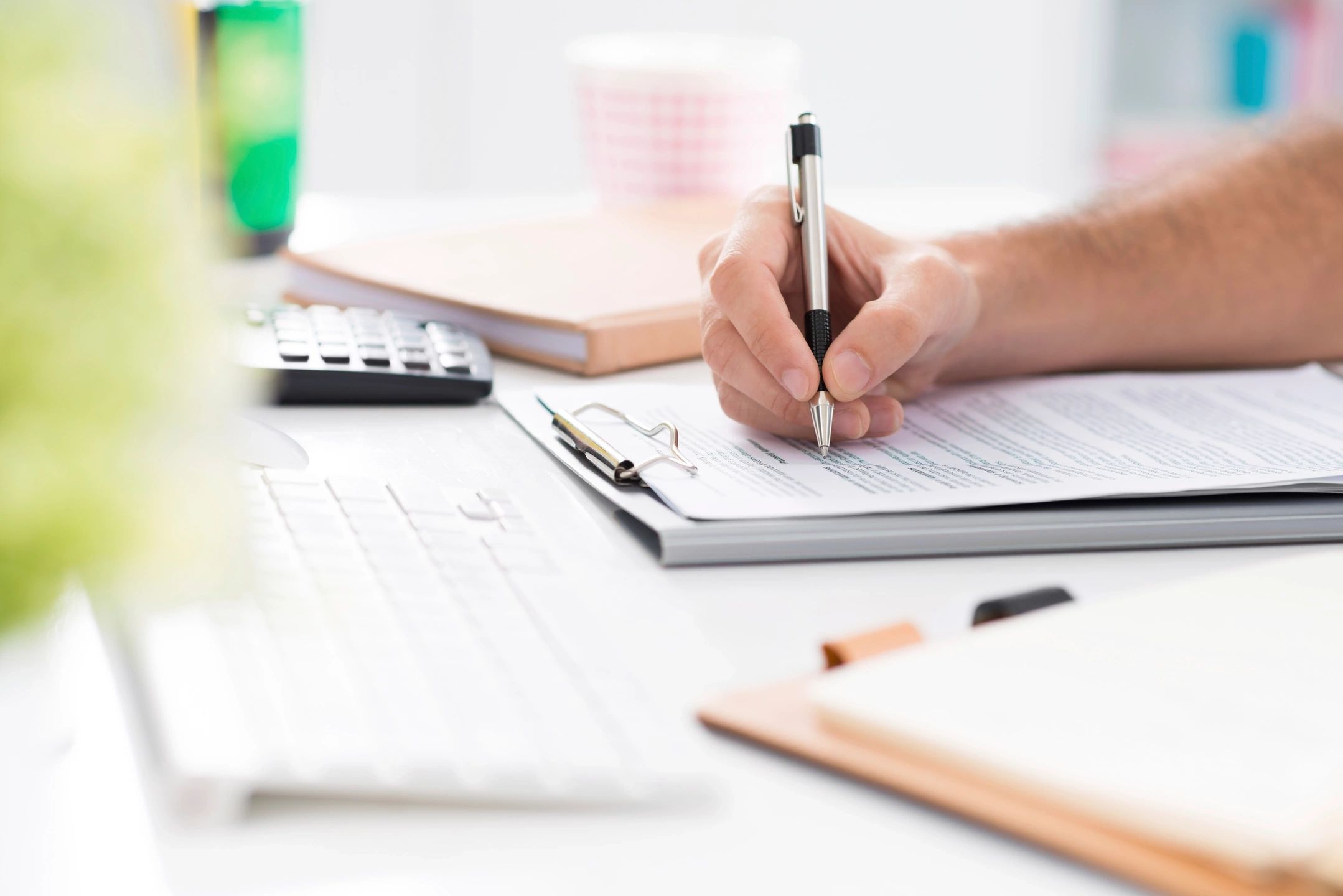 A view of a table with a person’s hand holding a pen and writing on a form