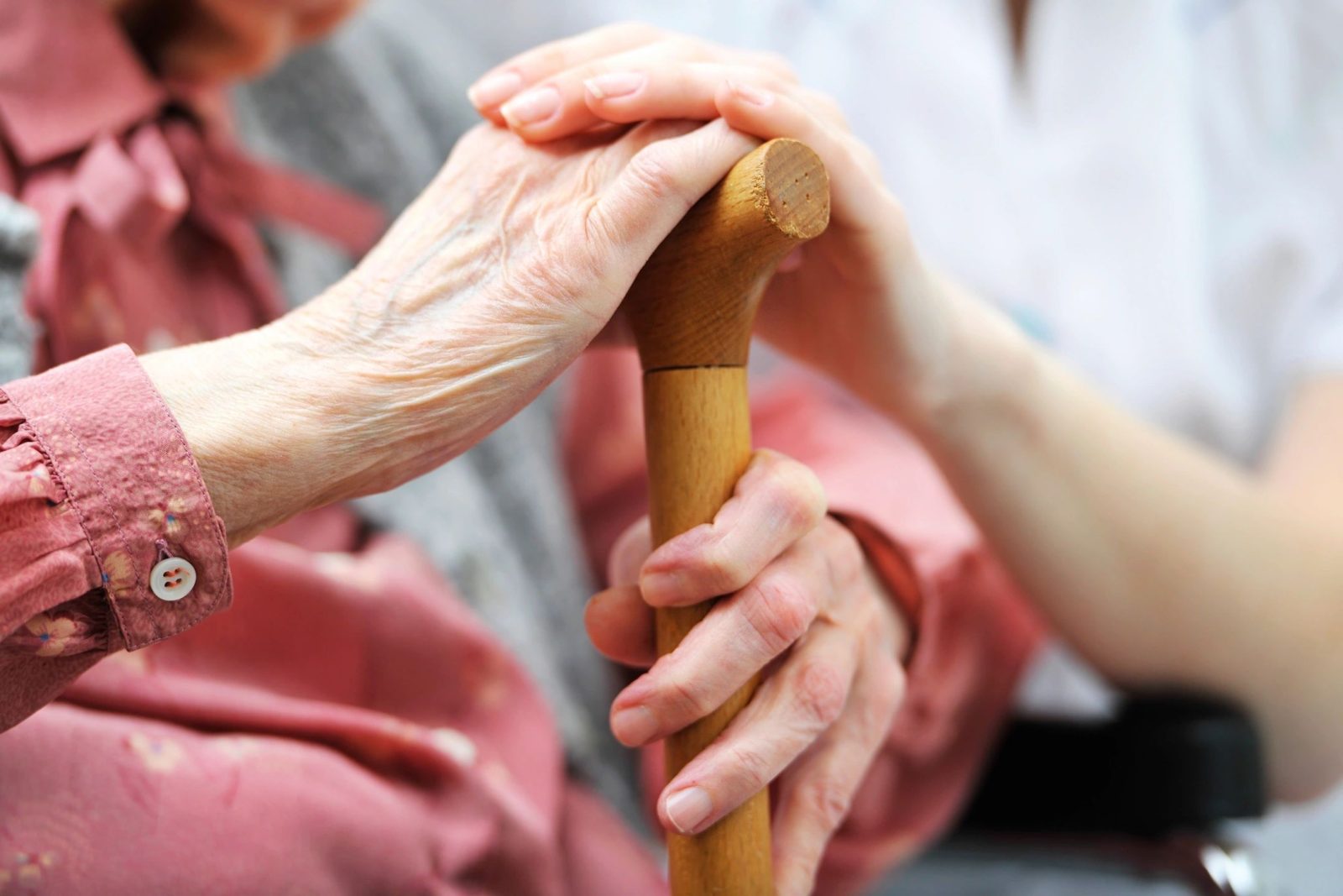 Elderly hand with cane, receiving support.